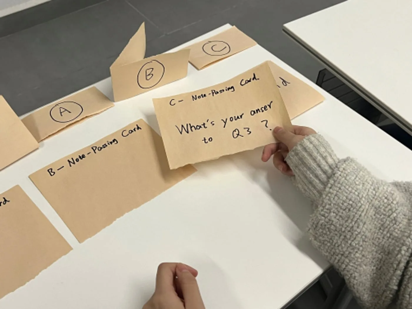 A hand sliding a paper note reading What's your answer to Q3 across the desk