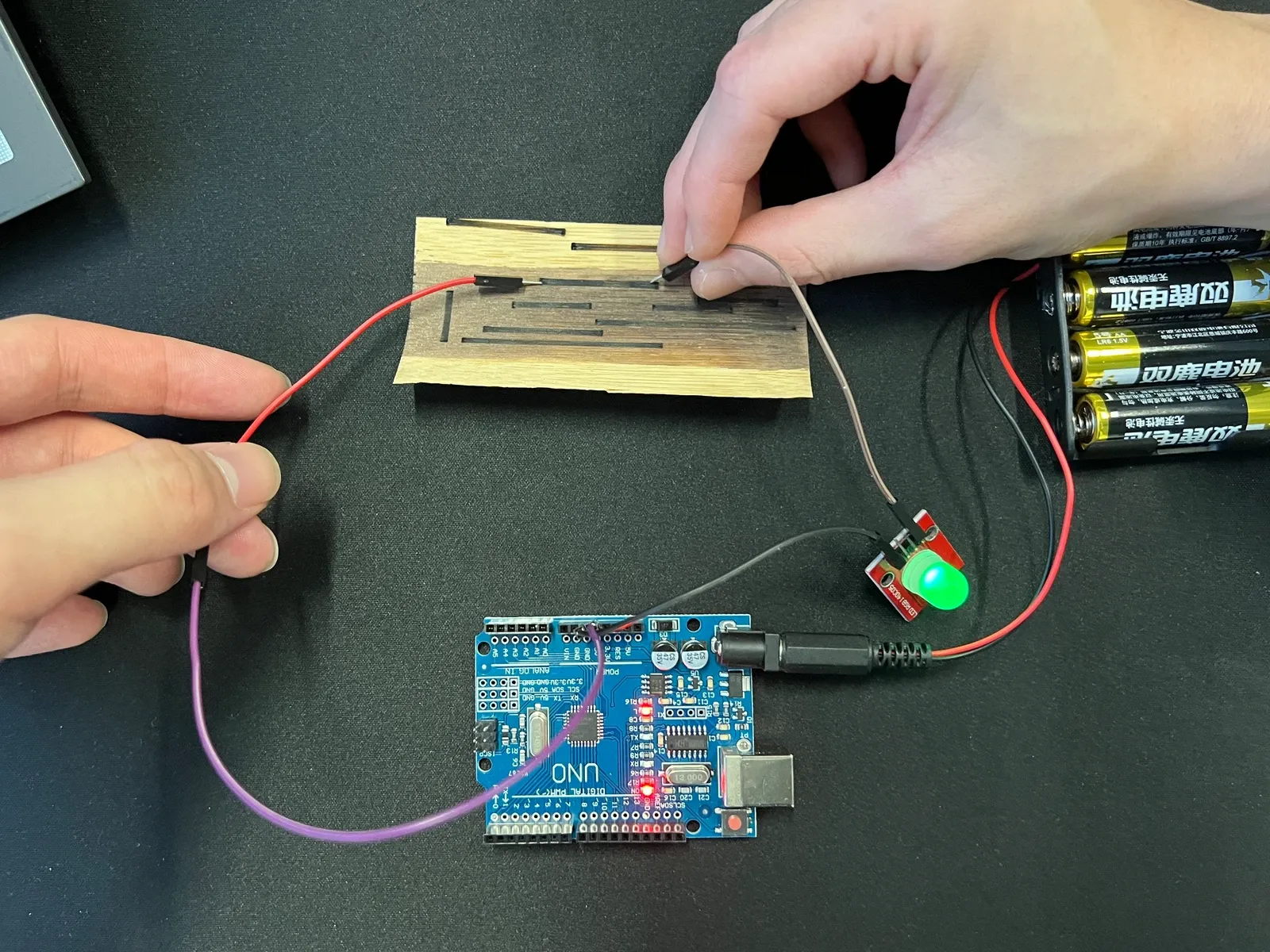 Hands touching a processed wood sample connected to an Arduino and an LED